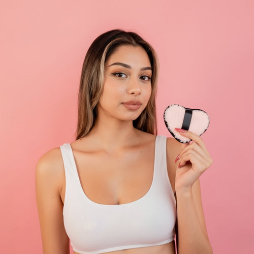 Woman holding a heart-shaped compact mirror against a pink background