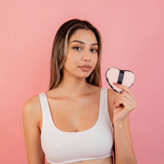 Woman holding a heart-shaped compact mirror against a pink background