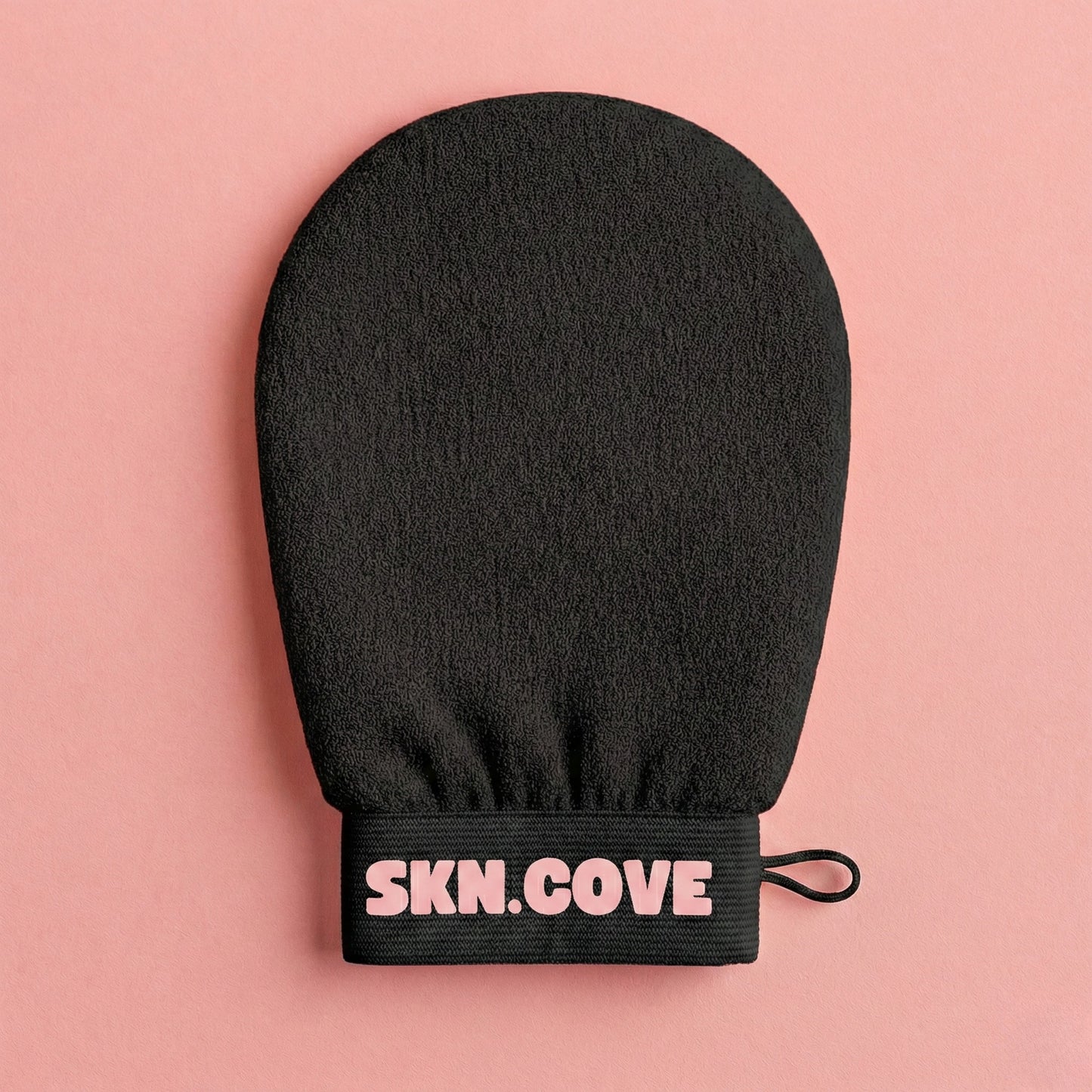Black exfoliating glove with 'SKN.COVE' branding on a pink background