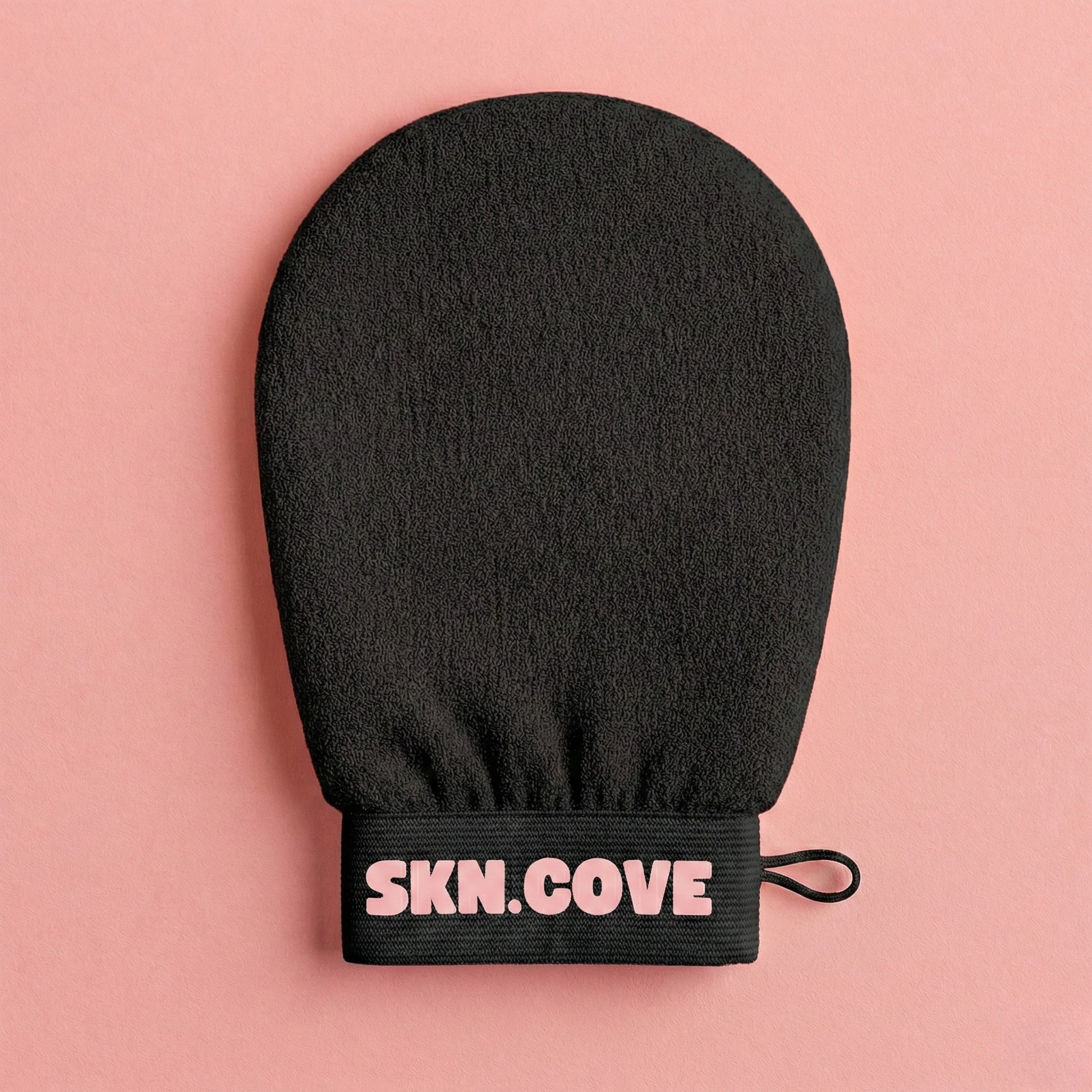 Black exfoliating glove with 'SKN.COVE' branding on a pink background