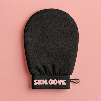 Black exfoliating glove with 'SKN.COVE' branding on a pink background