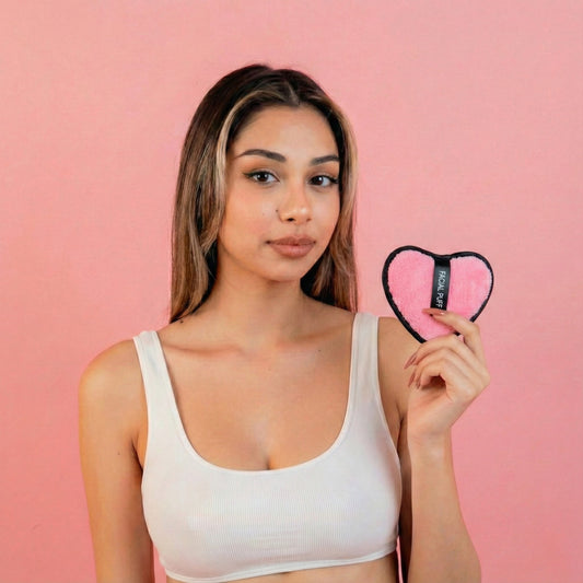 Woman holding skncove pink heart-shaped makeup eraser product against a pink background