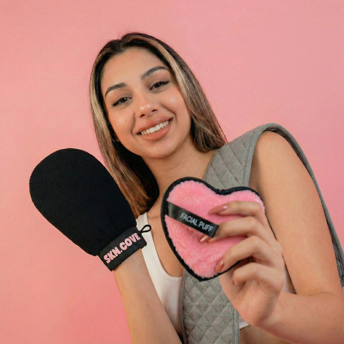 Woman holding the SknCove black exfoliating glove and heart makeup puff