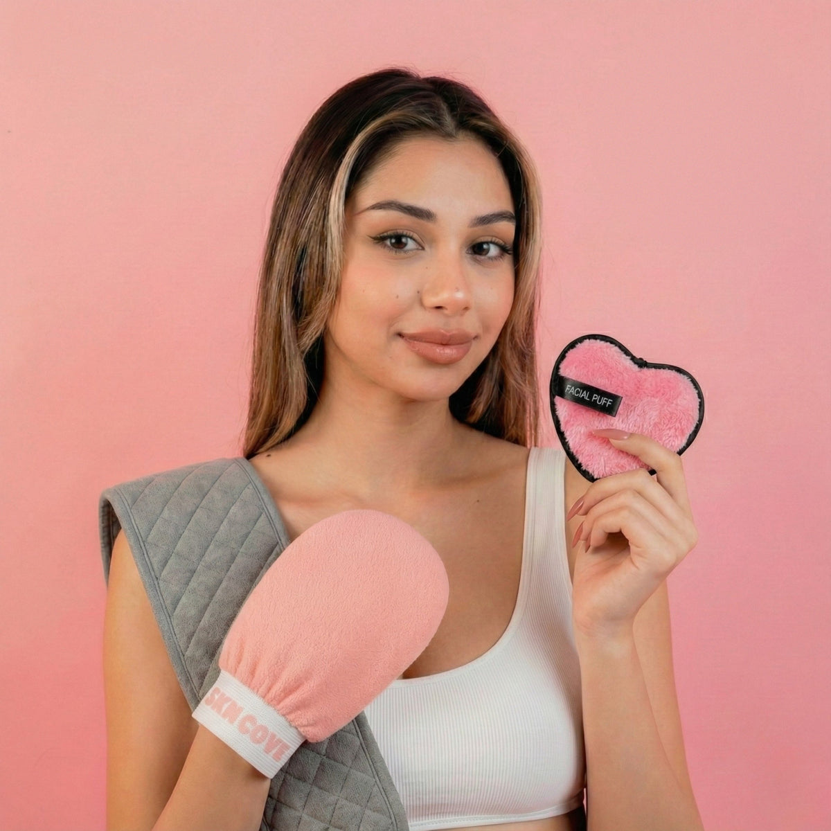 Woman holding the SknCove back scrubber belt, exfoliating glove and heart puff