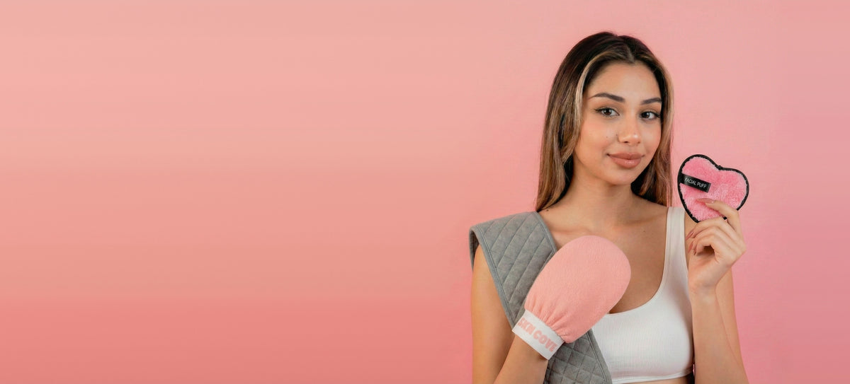 Woman holding the SknCove Full Body Glow Kit: exfoliating glove, back scrubber belt and heart makeup puff